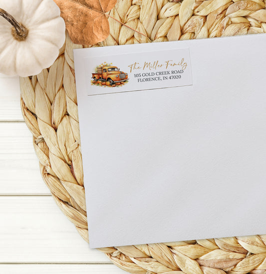 White envelope with fall-themed address label on a woven mat with pumpkins.
